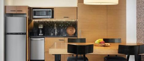 A modern kitchen with a built-in microwave, stainless steel refrigerator, and a wooden dining table with black chairs.