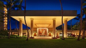 Entrada de hotel con un amplio arco central, palmeras y una fachada bien iluminada.
