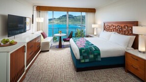 Habitación de hotel con cama, escritorio, silla, televisor, balcón y vistas a la ciudad.