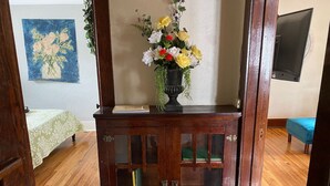 Een houten kast met glazen deuren, een vaas met bloemen, een boek en een schilderij aan de muur.