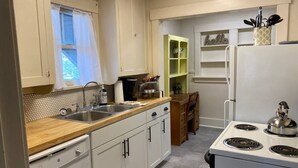 Een keuken met witte kastjes, een houten aanrecht, een spoelbak, een fornuis en een raam met gordijn.