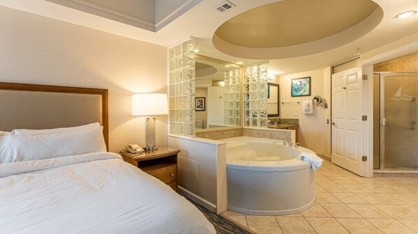 A hotel room with a bed, a nightstand, a bathroom with a bathtub, a mirror, and a shower.
