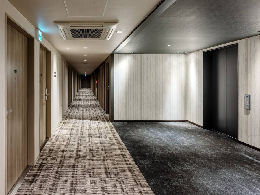 Un pasillo de hotel con piso alfombrado, puertas de madera y un ascensor moderno.