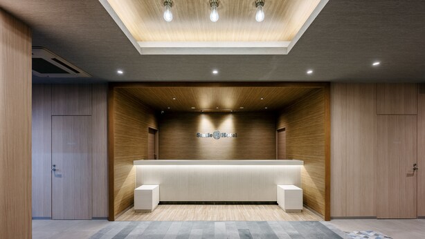 A reception area with a reception desk, wooden panel walls, and a patterned floor. - Smile Hotel Okayama (Okayama)