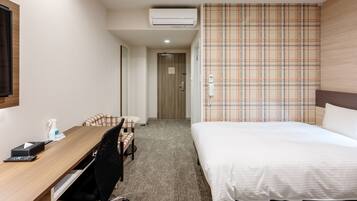 A hotel room with a wooden desk, a bed, a plaid-patterned curtain, and an air conditioning unit.