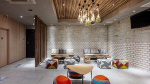 A modern lounge area with a wooden ceiling, recessed lighting, and a variety of seating options including sofas, chairs, and colorful ottomans. - Smile Hotel Okayama (Okayama)
