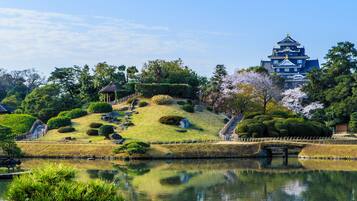 A traditional Japanese castle with a reflection in a pond, surrounded by well-maintained gardens and cherry blossoms.