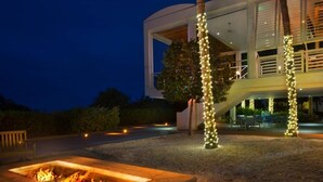 Una casa moderna con un pozo de fuego, asientos exteriores e iluminacion con luces colgantes.