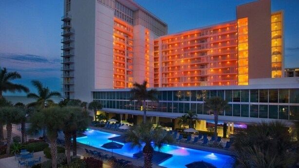 Un hotel de varios pisos, piscina y palmeras.
