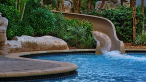 Una piscina con tobogán de agua, rodeada de exuberante follaje y rocas.
