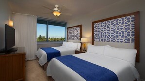 Habitación de hotel con dos camas, televisor, ventilador de techo y ventana con vistas a zonas verdes.