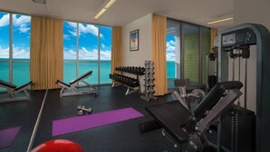 Un gimnasio con equipo de ejercicio, colchonetas de yoga y vistas al océano.
