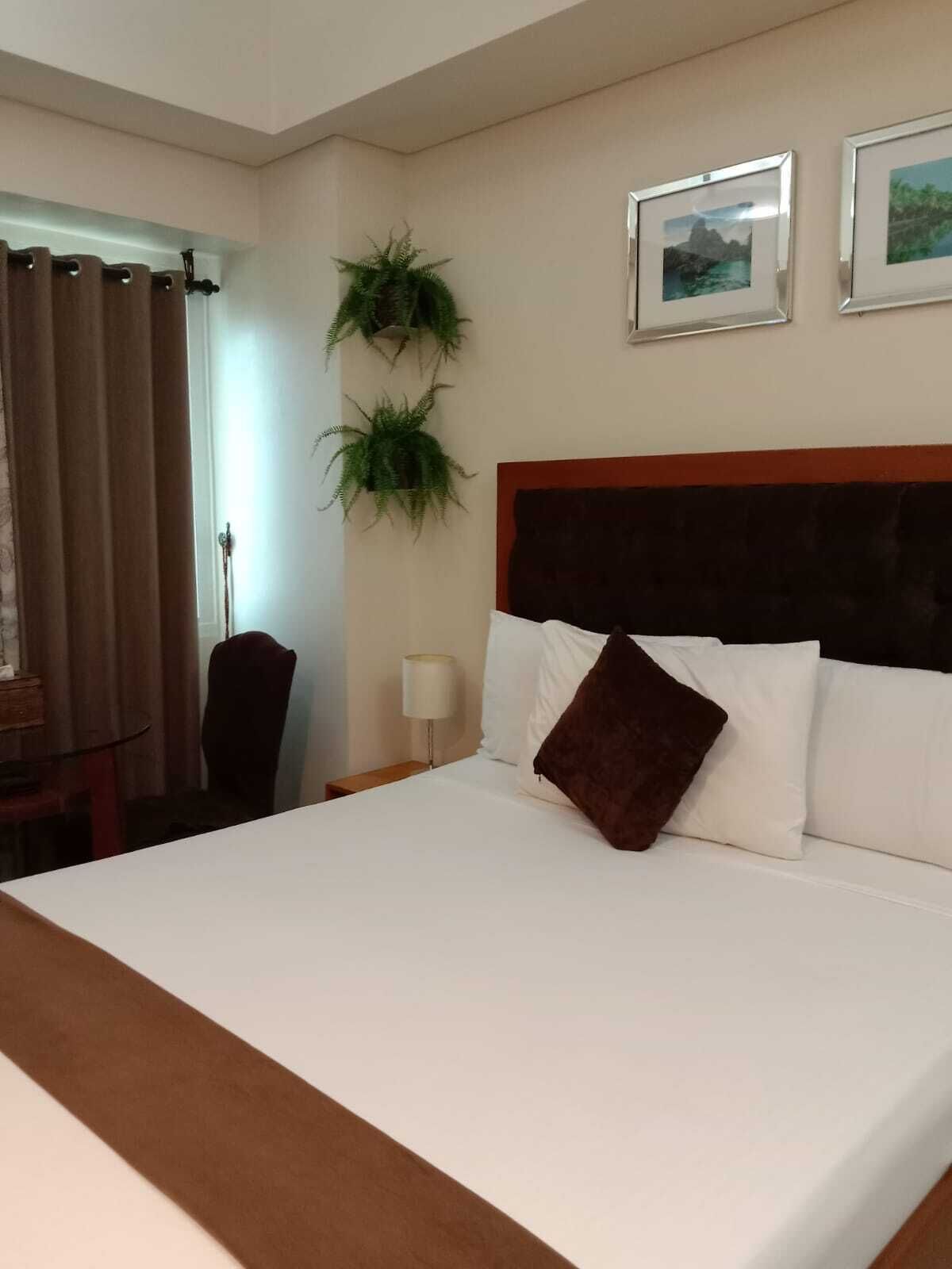 A hotel room with a large bed, a wooden headboard, two wall-mounted plants, and framed pictures.