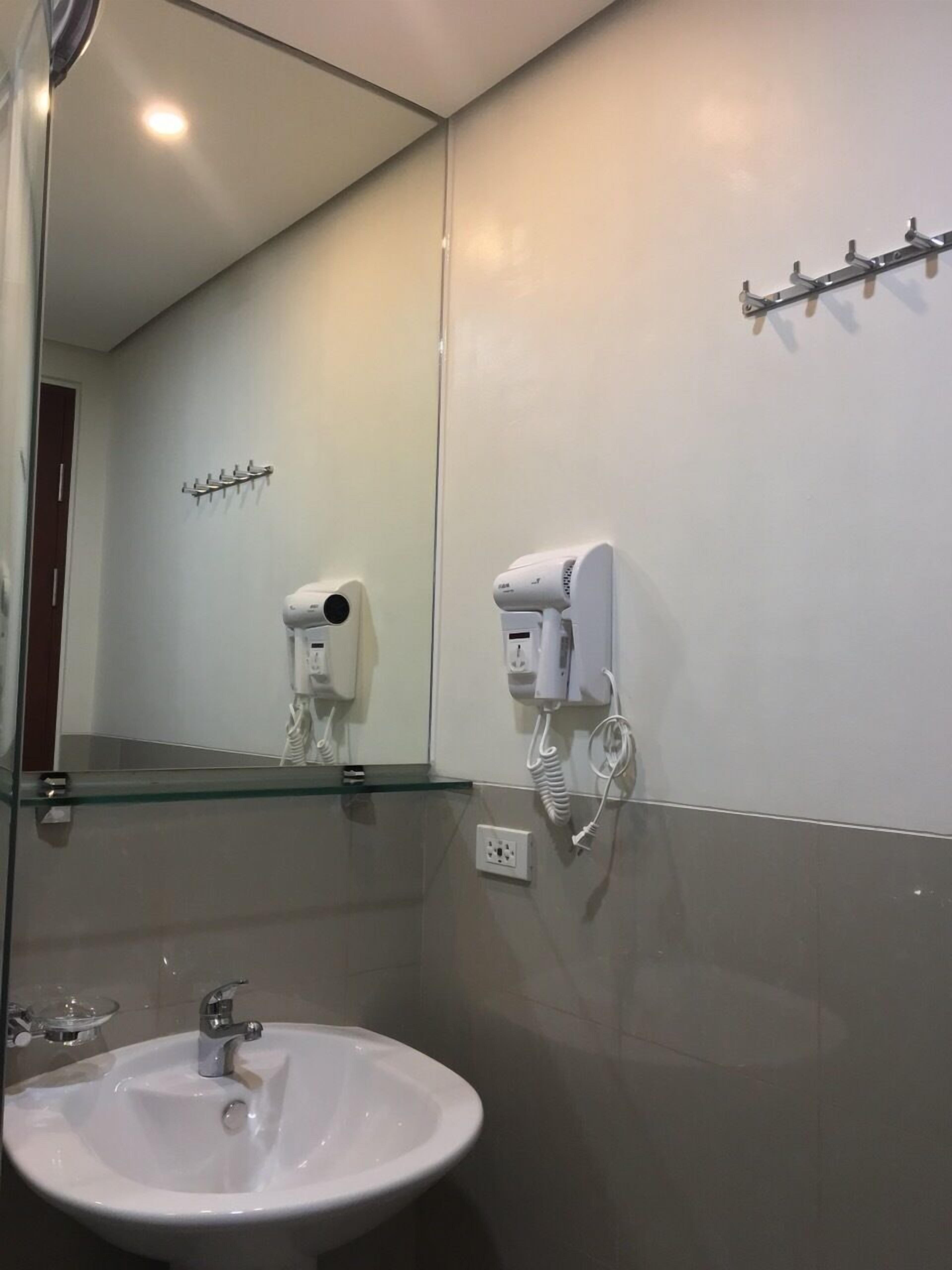 A bathroom with a white sink, a mirror, and a hairdryer mounted on the wall.