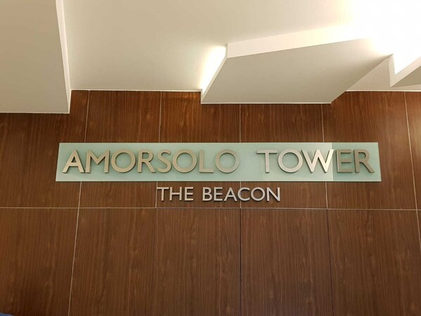 A sign for Amorsolo Tower, The Beacon, with a wooden panel background and a light fixture above. - Studio Unit at The Beacon Makati (Makati)