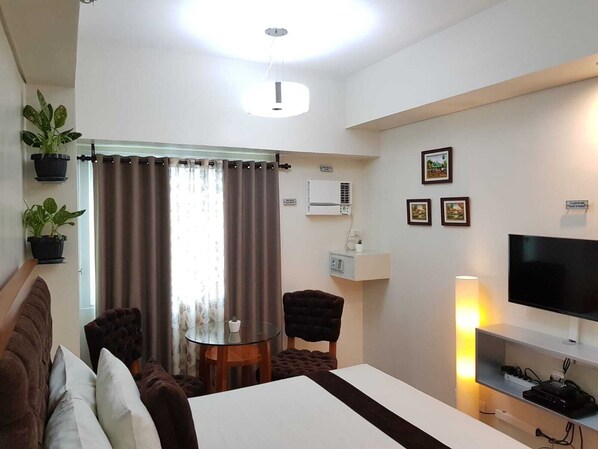 A hotel room with a bed, a TV, a desk, and a chair. There are potted plants on the windowsill and a curtain. - Studio Unit at The Beacon Makati (Makati)