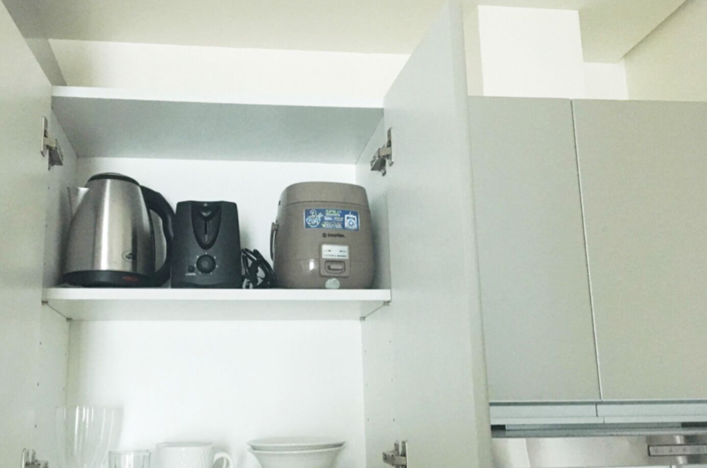 A kitchen with a shelf holding a kettle, a coffee maker, and a rice cooker.