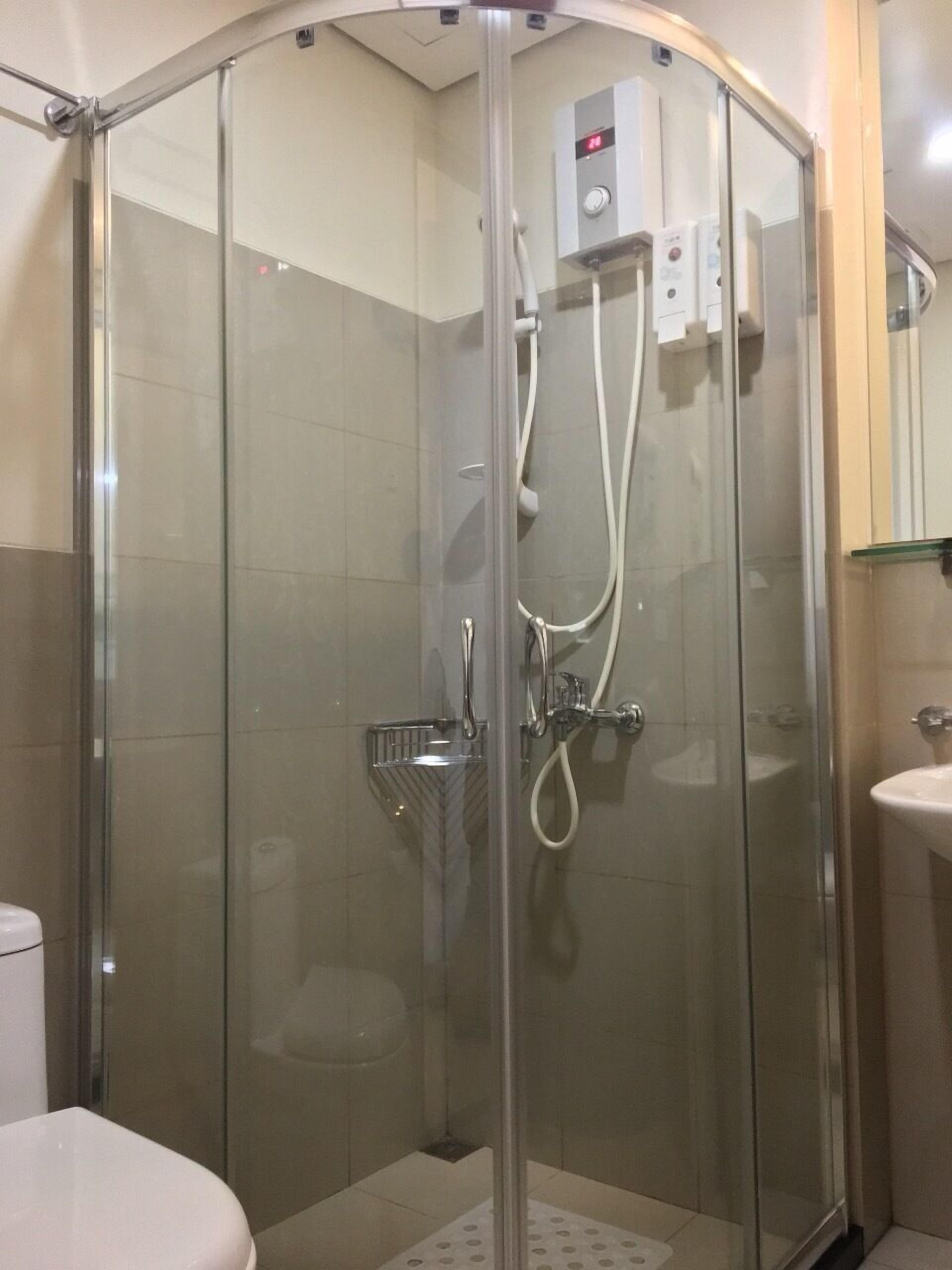 A glass-enclosed shower stall with a control panel above the door, a handheld showerhead, and a handheld faucet.