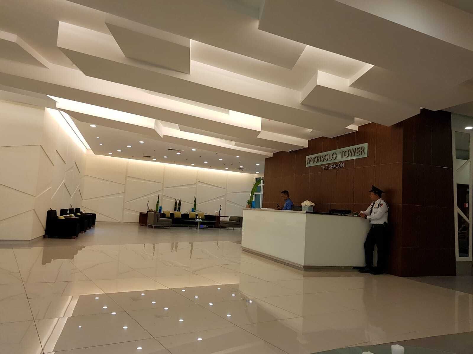 A modern hotel lobby with a reception desk, seating area, and a sign reading "Amorsolo Tower The Beacon".