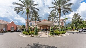 A hotel entrance with palm trees, a fountain, and a clear sky.