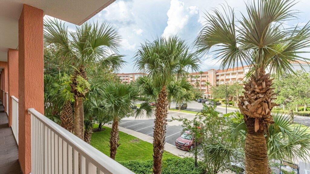 Ein Balkon mit Palmen, ein Parkplatz und ein Gebäude im Hintergrund.