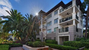 A multi-story building with balconies, surrounded by well-maintained gardens and palm trees.