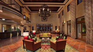 A spacious lobby with a high ceiling, a central seating area with sofas and armchairs, a reception desk, and a large chandelier.