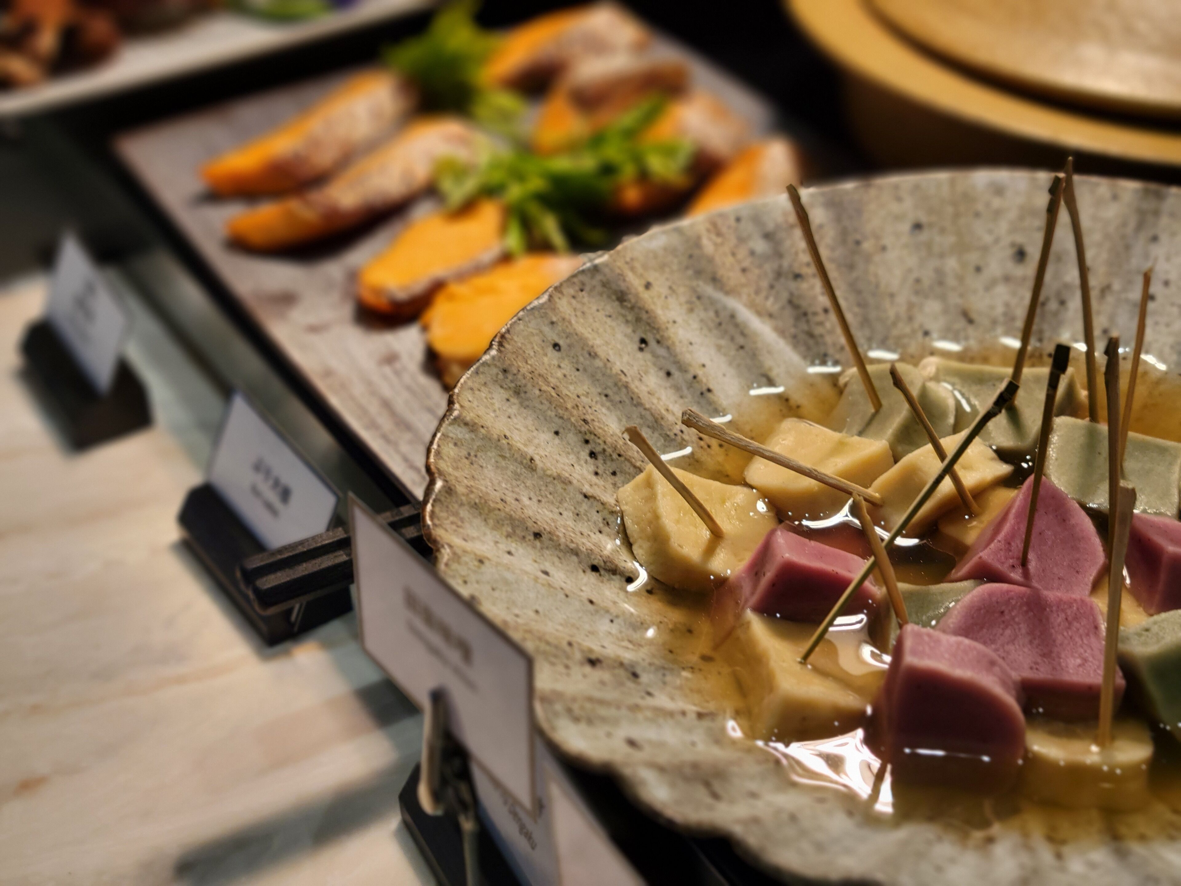 A ceramic dish with various food items, including cubes of meat and vegetables, and a liquid base.