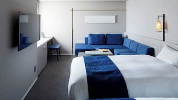 A modern hotel room with a large bed, a sofa, a desk, and a television.
