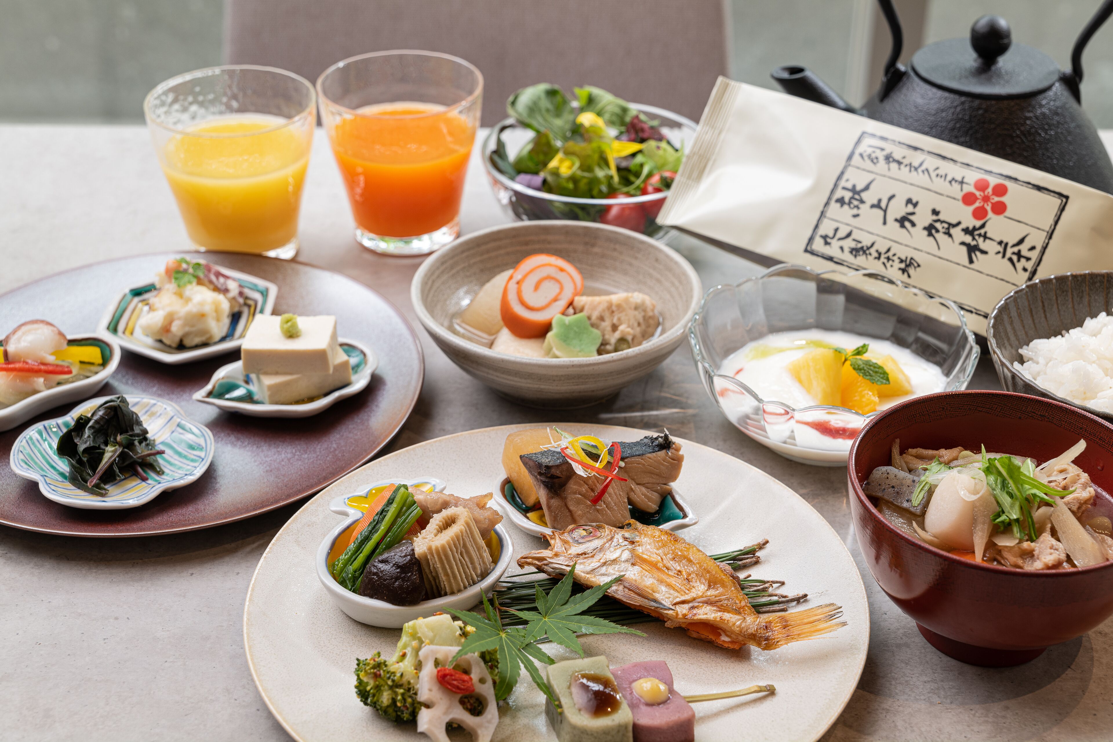 A variety of dishes including a fish, tofu, and vegetables, along with two glasses of orange juice.