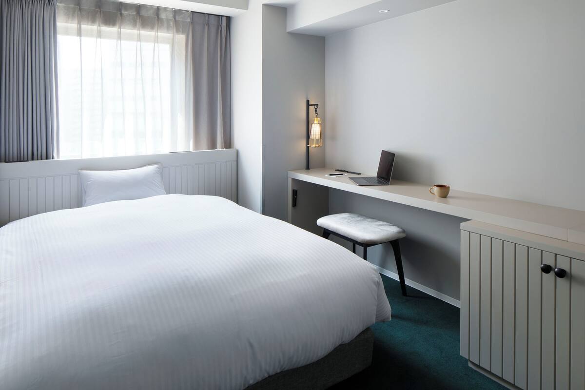 A hotel room with a large bed, a desk with a laptop, a chair, and a cabinet.
