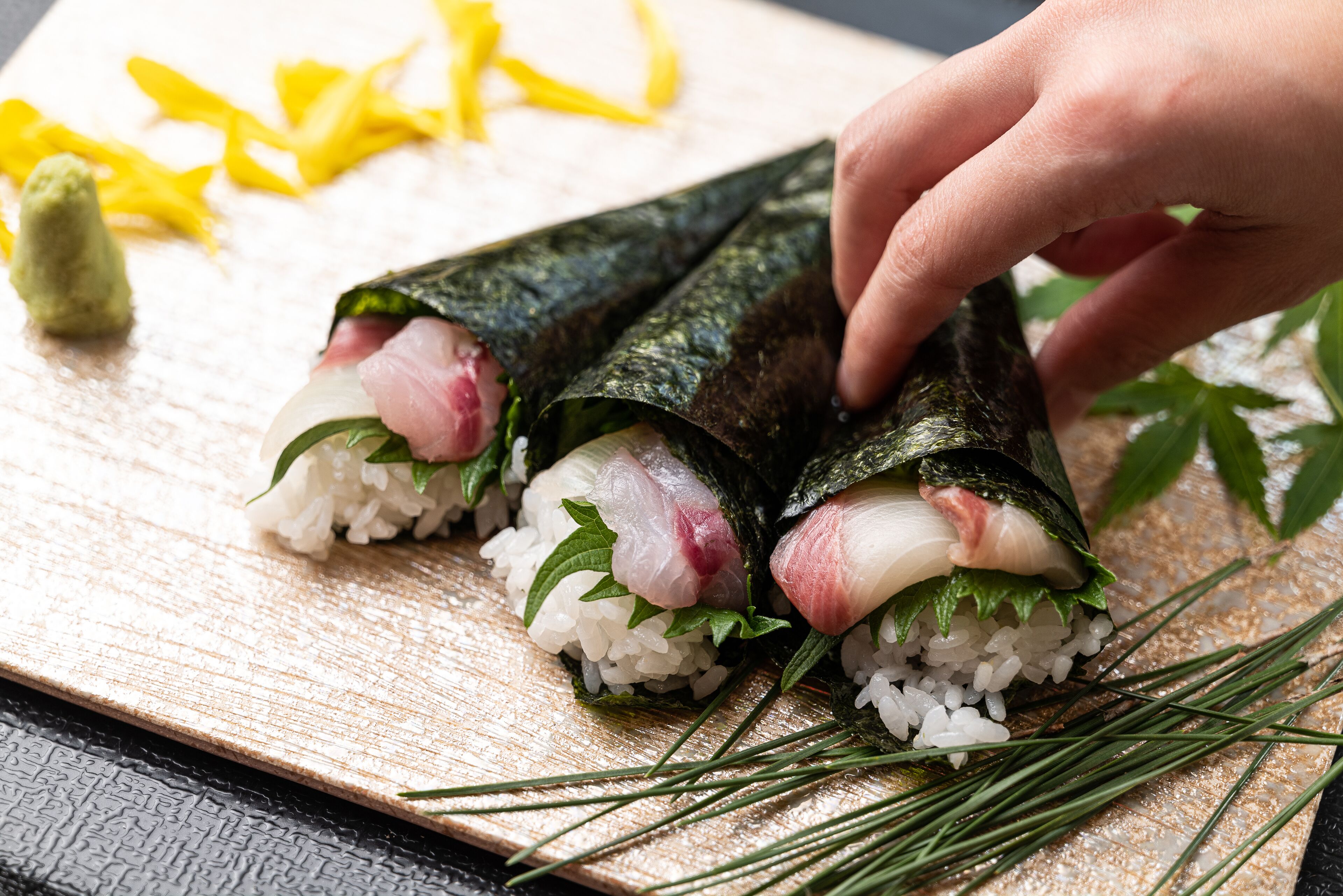 Sushi rolls on a wooden board with a hand placing a roll.