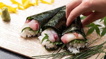 Sushi rolls on a wooden board with a hand placing a roll.