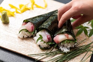 Rollos de sushi sobre una tabla de madera, con una mano colocando uno.