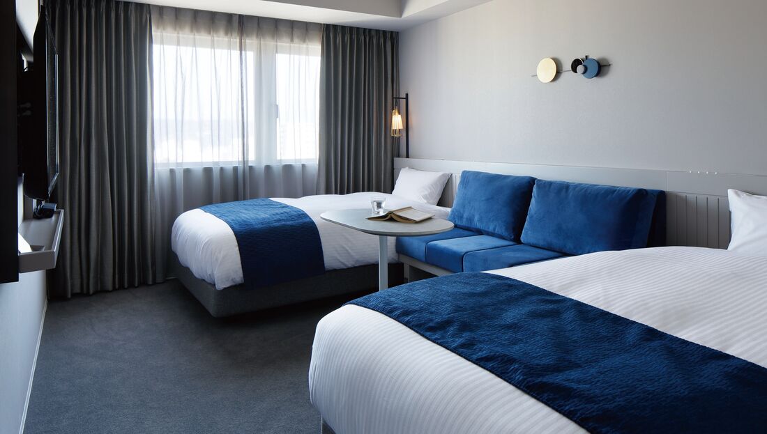 Une chambre d’hôtel avec un lit, un canapé, une petite table et une fenêtre avec des rideaux.