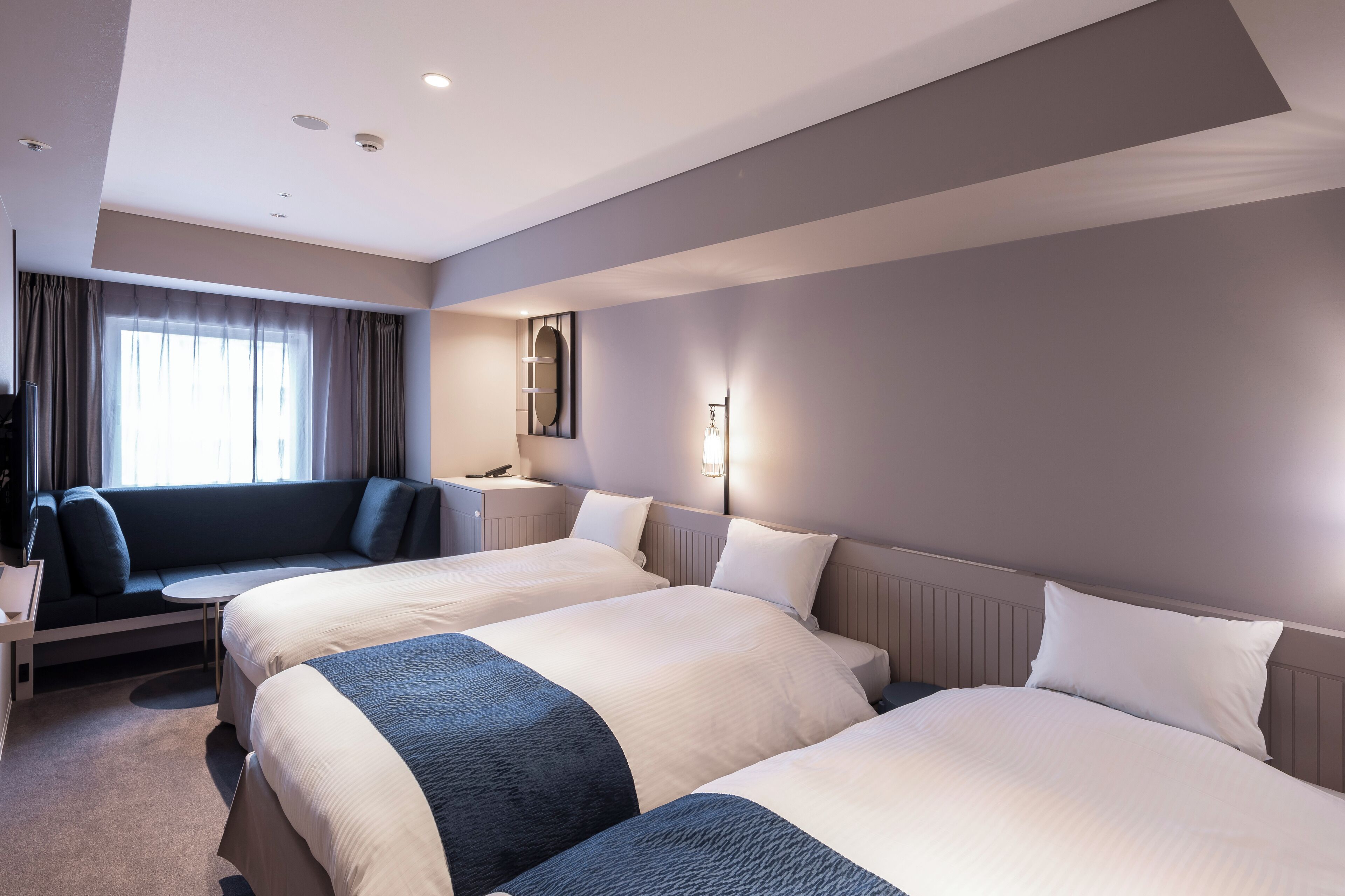 Habitació d'hotel amb dos llits, un sofà, un escriptori i una finestra amb cortines.