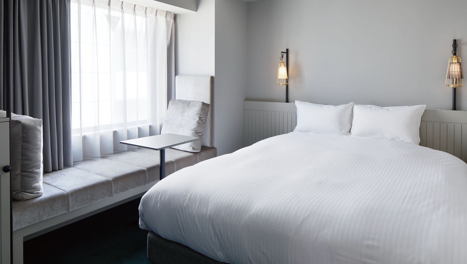 Une chambre d’hôtel avec un grand lit, une petite table, une chaise et deux lampes fixées au mur.