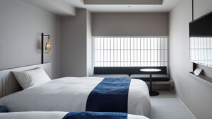 Een moderne hotelkamer met een groot bed, een klein rond tafeltje, een bankje en een aan de muur bevestigde televisie.