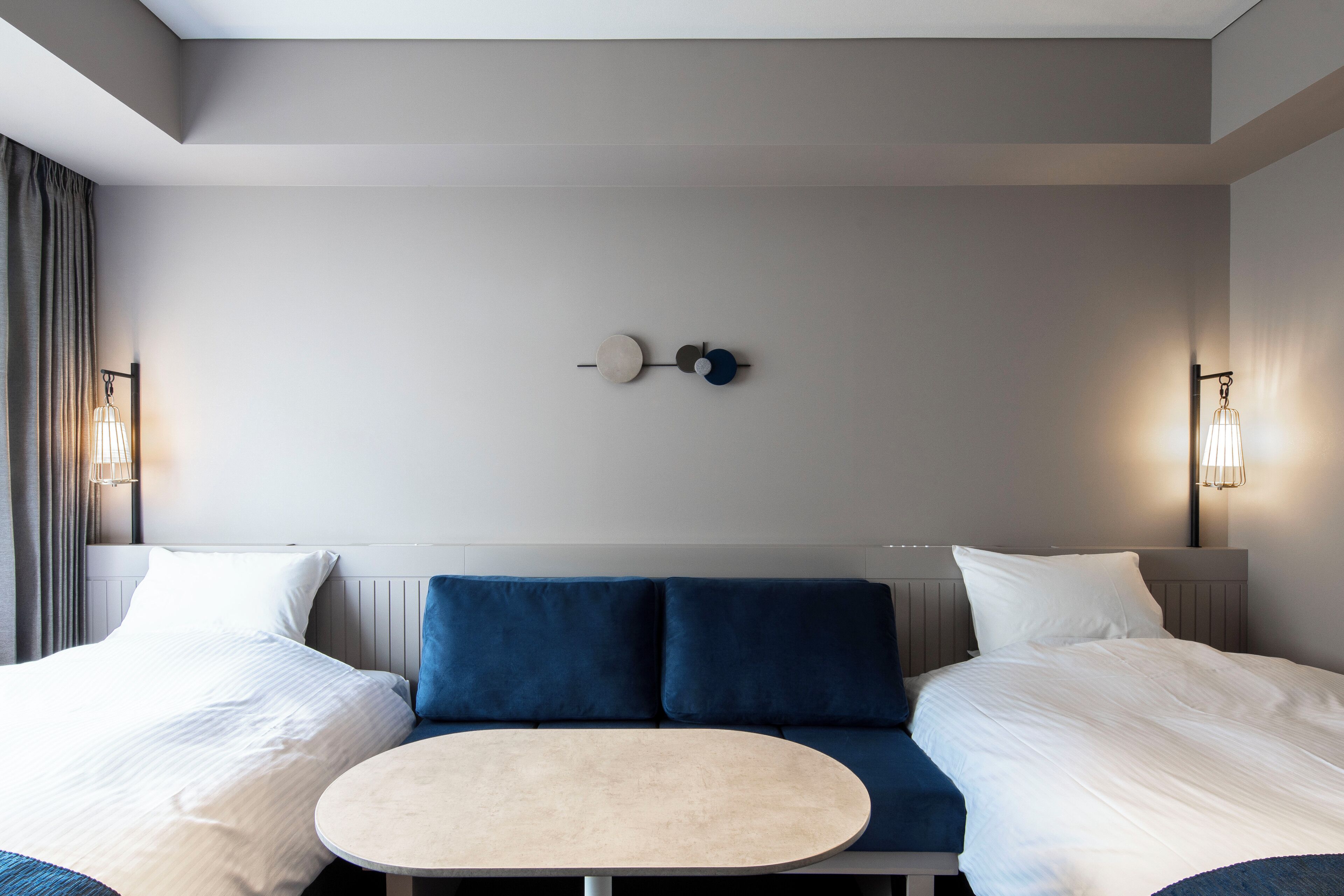 A modern hotel room with a double bed, a round table, and two blue accent pillows.
