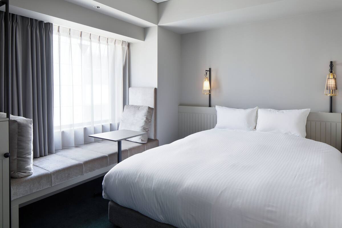 A hotel room with a large bed, a seating area with a table, and two wall-mounted lamps.