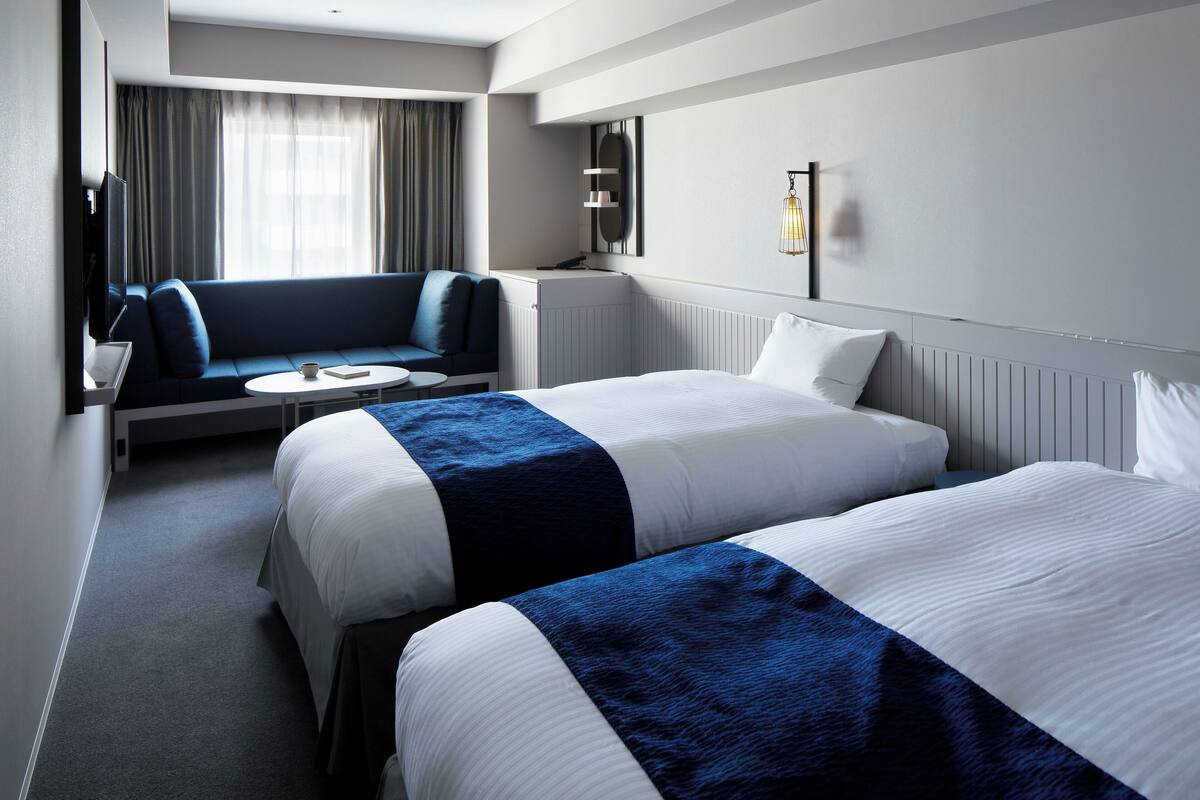 A hotel room with two beds, a sofa, a small round table, and a TV.