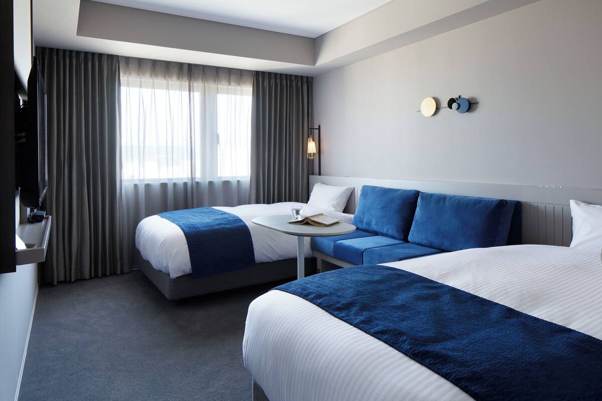 A hotel room with two beds, a sofa, a small table, and a TV.