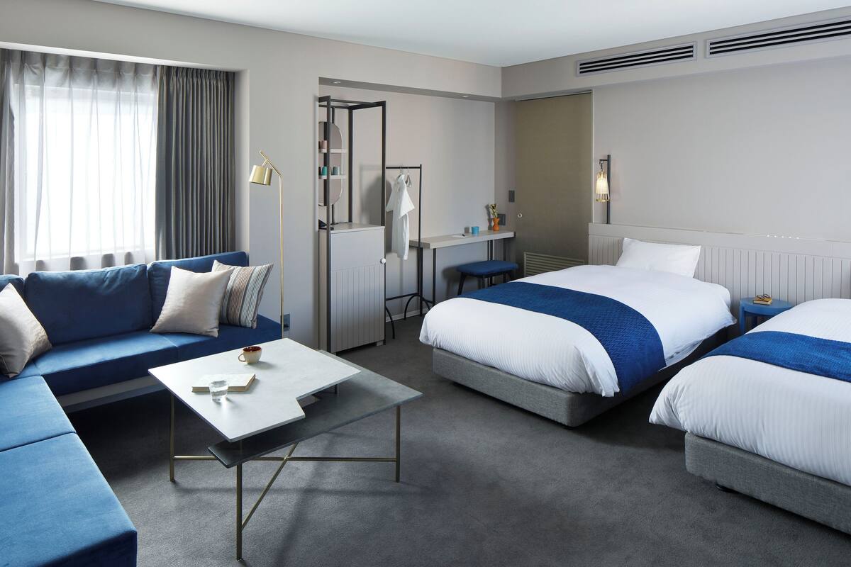 A hotel room with a sofa, two beds, a desk, and a mirror.