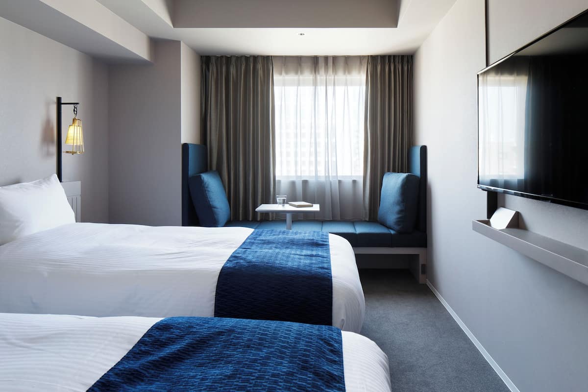 A hotel room with two beds, a TV, a small table, and a sofa.