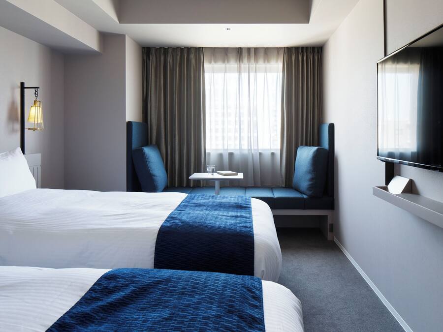 Quarto de hotel com duas camas, uma televisão, uma mesinha e um sofá.