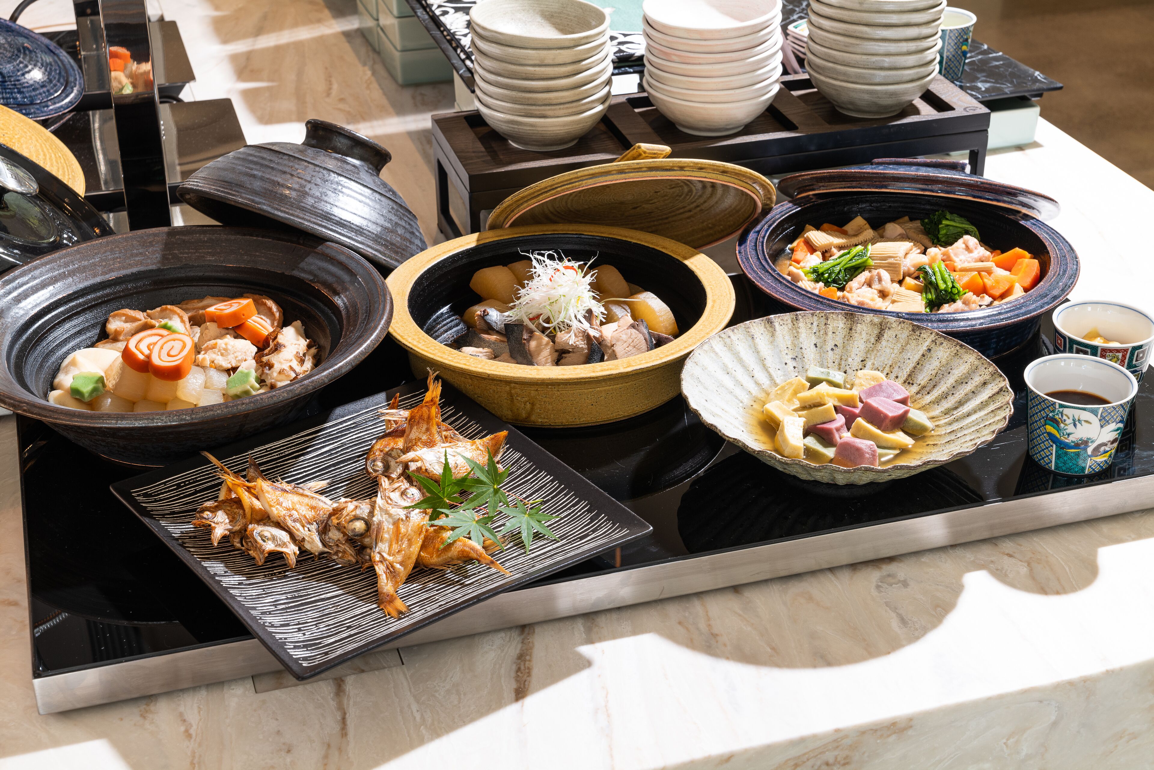 A variety of dishes on a table, including seafood, vegetables, and possibly meat, with bowls and plates arranged around a central heating element.