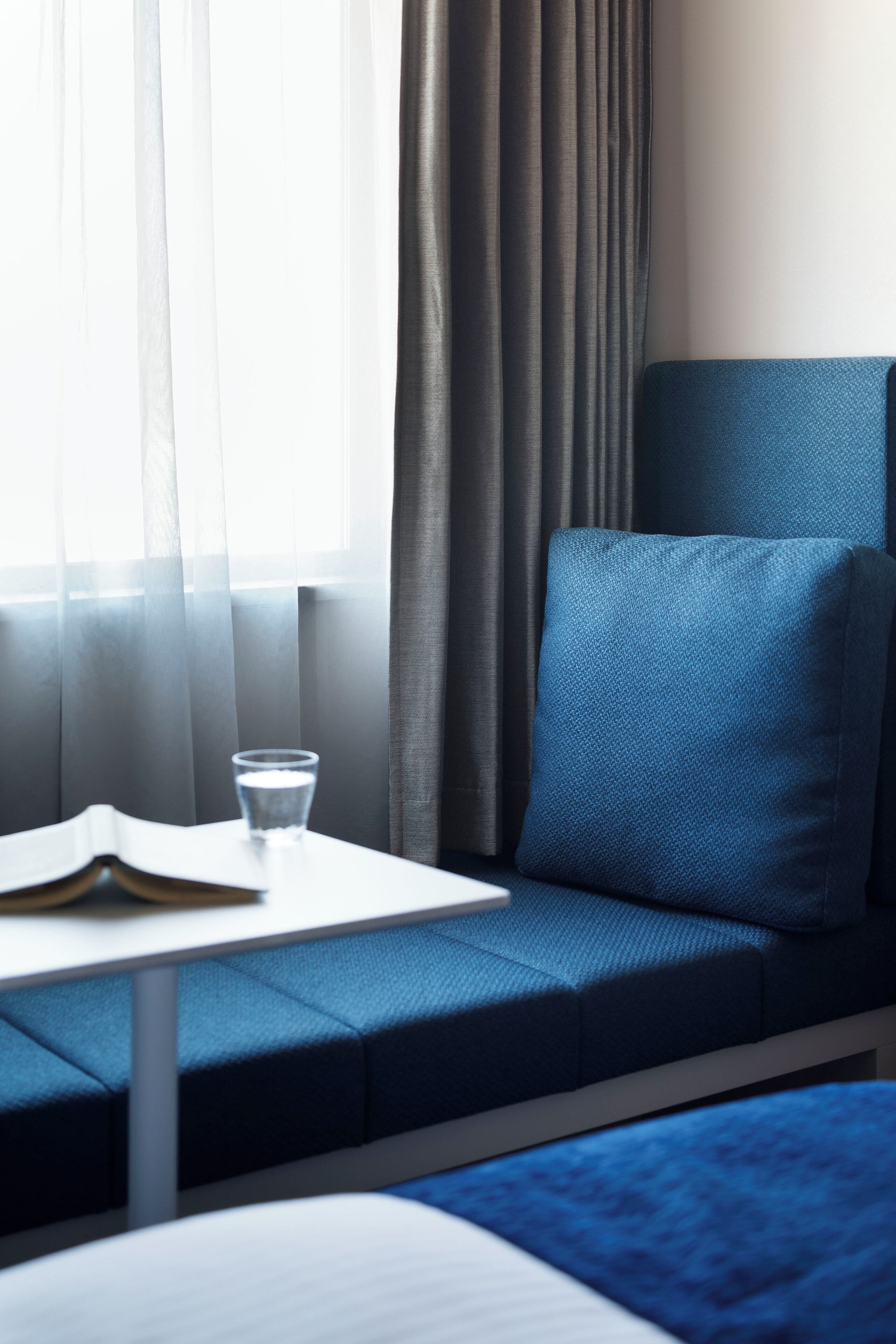 A modern hotel room with a blue sofa, a small table, and a glass of water.