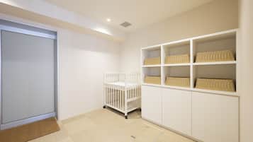 A room with a white crib, white shelving with wicker baskets, and a beige carpet.