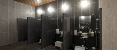 A modern bathroom with dark tiled walls, wooden ceiling panels, and individual shower cubicles.