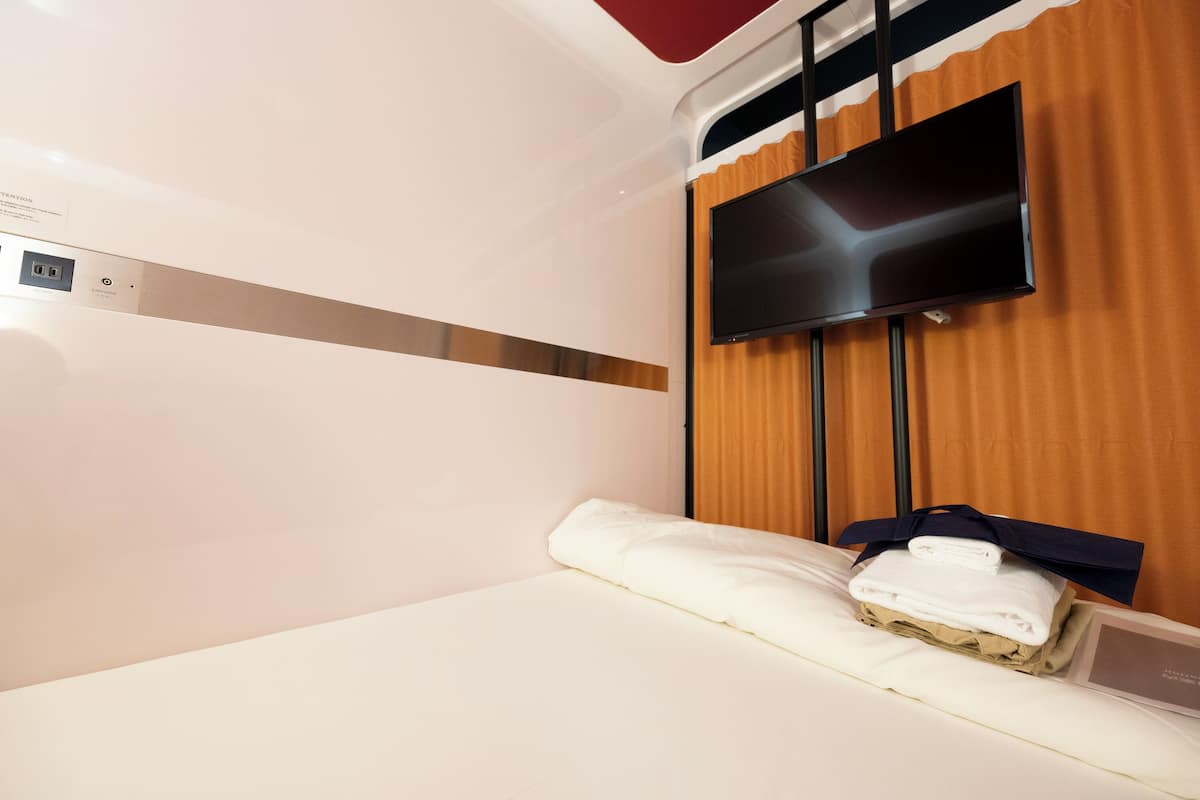 Habitación de hotel con cama, televisor de pantalla plana montado en la pared y toma de corriente.